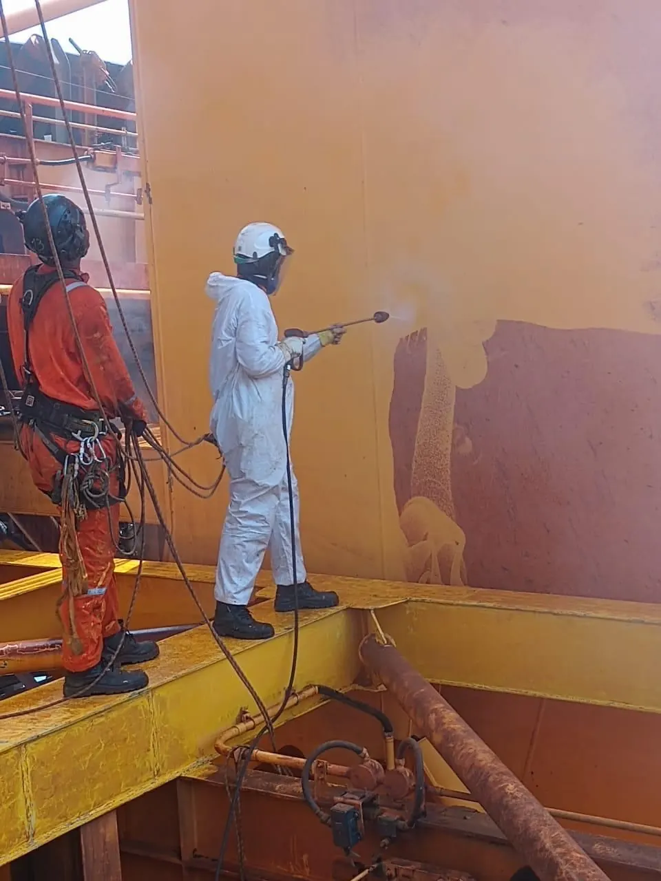 Hidrojateamento em chapa de equipamento industrial, com operador de macacão branco